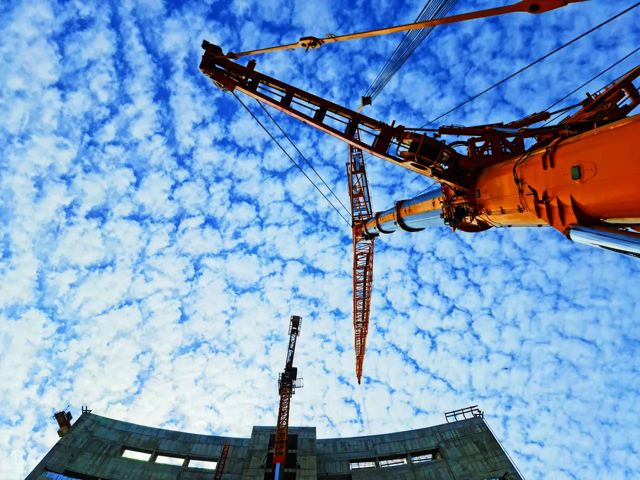 Crane boom and jib against a vivid blue cloud-patterned sky