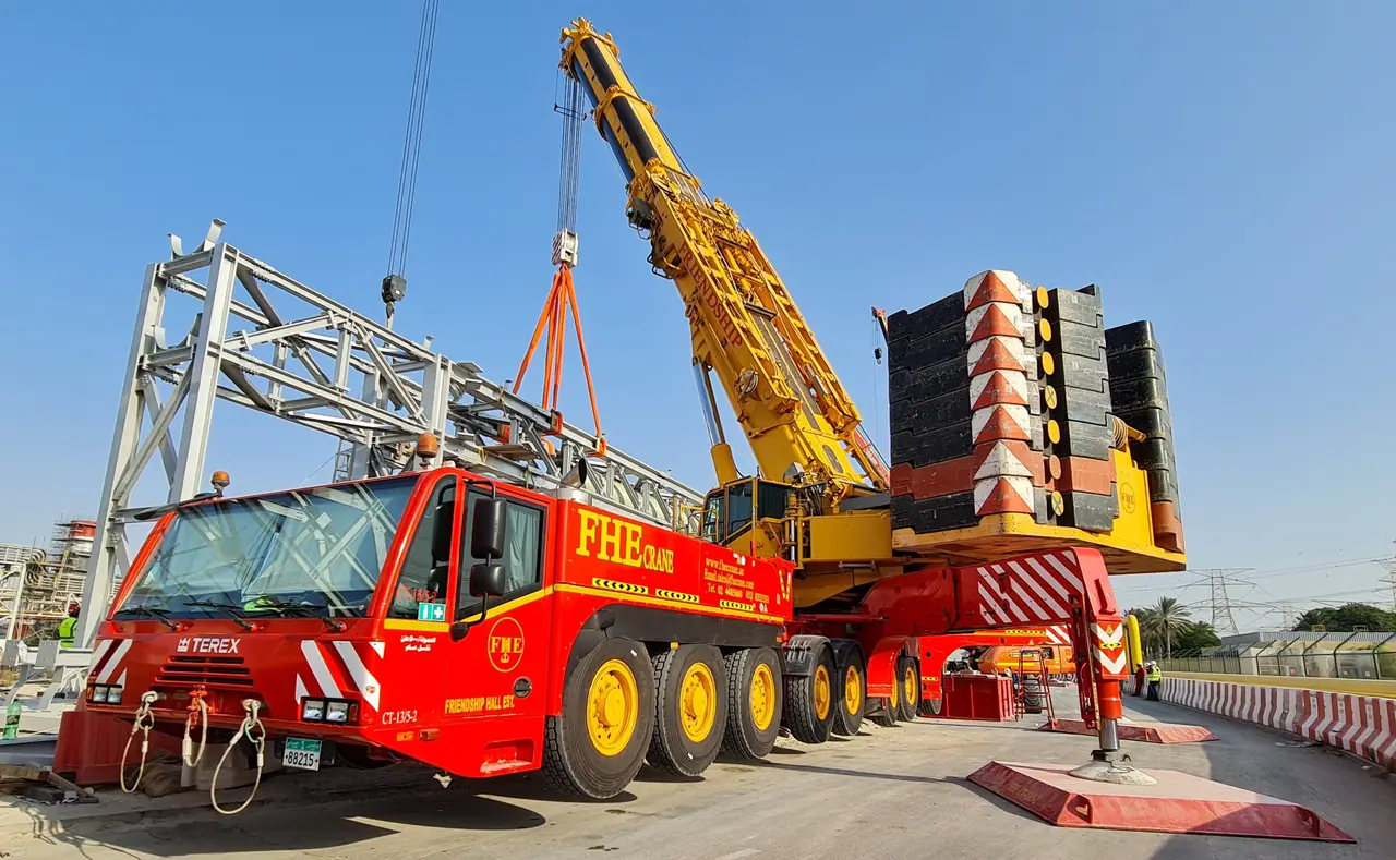 Red FHE crane with counterweight stack lifting a steel truss