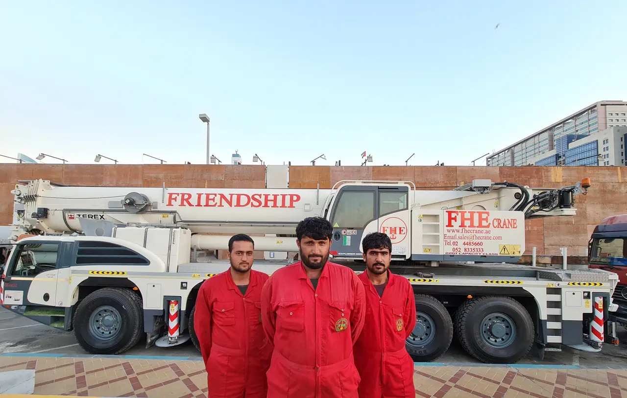 Three FHE crew in red coveralls in front of a Terex FRIENDSHIP crane