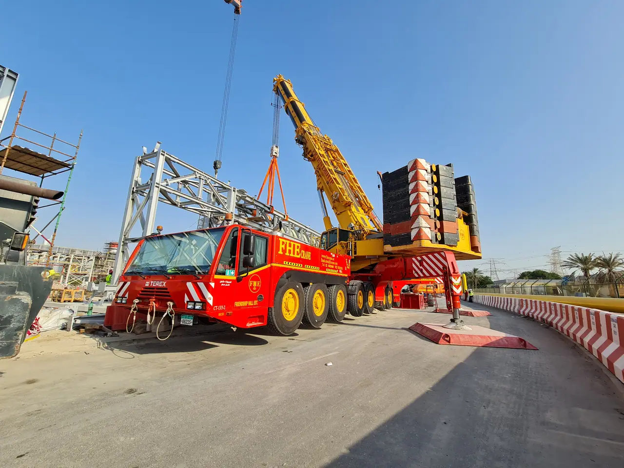 Red FHE heavy crane with superlift counterweight lifting a steel truss