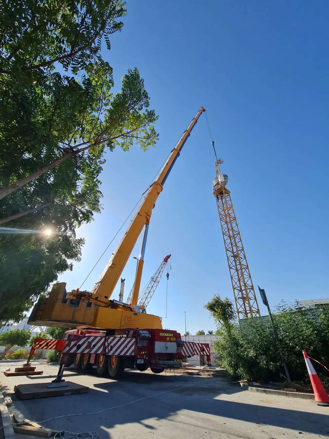 Yellow mobile crane working beside a tower crane on a tree-lined site